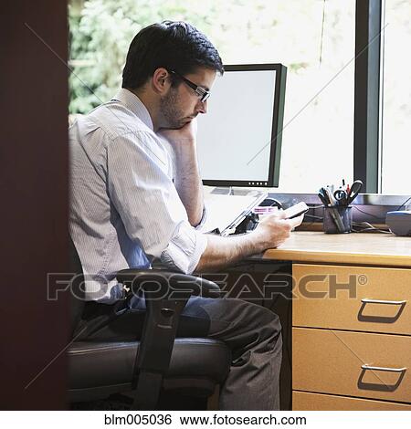 Stock Photograph - Hispanic businessman at desk looking at cell phone. Fotosearch