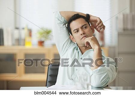 Picture - Hispanic businessman sitting at desk thinking. Fotosearch