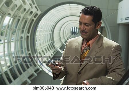 Stock Image - Hispanic businessman text messaging on cell phone. Fotosearch