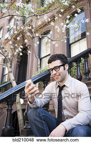 Stock Photo - Hispanic businessman using cell phone on front steps. Fotosearch
