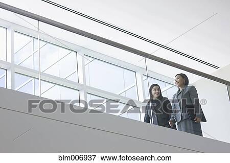 Stock Photo - Hispanic businesswomen talking on balcony. Fotosearch