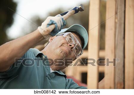 Stock Image - Hispanic construction worker using hammer on house frame. Fotosearch