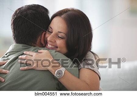 Stock Image - Hispanic couple hugging on sofa. Fotosearch
