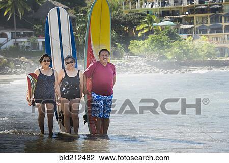 Stock Image - Hispanic friends with surfboards on beach. Fotosearch