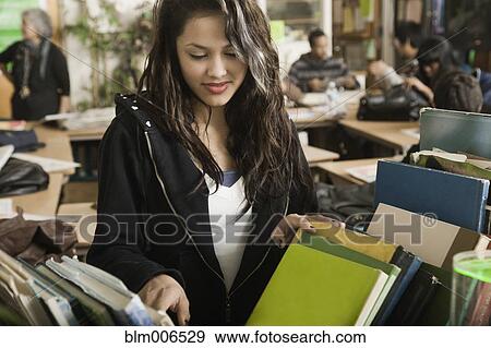 Stock Photo - Hispanic girl looking for book in classroom. Fotosearch
