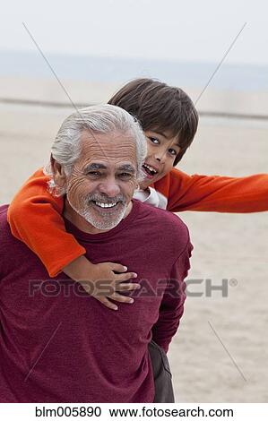 Stock Image - Hispanic grandfather giving grandson piggyback ride. Fotosearch