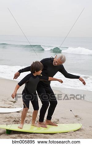 Stock Photography - Hispanic grandfather teaching grandson to surf. Fotosearch