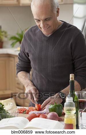 Stock Photo - Hispanic man chopping vegetables in kitchen. Fotosearch