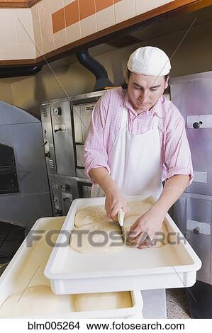 Picture - Hispanic man cutting pizza dough. Fotosearch