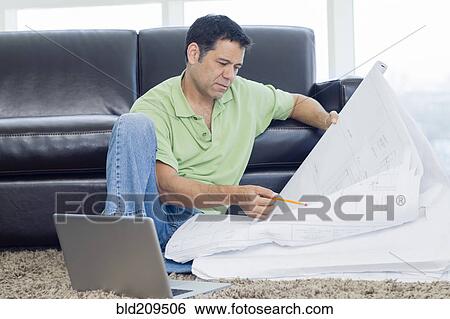 Stock Photograph - Hispanic man examining blueprints in living room. Fotosearch