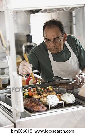 Hispanic man grilling meat in food cart View Large Photo Image Stock Photo - Hispanic man grilling meat in food cart. Fotosearch
