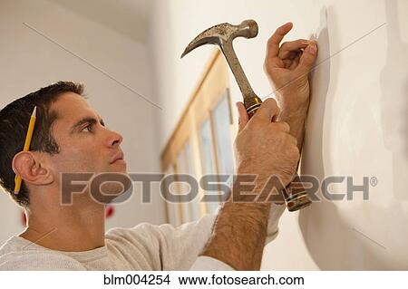 Hispanic man hammering nail into wall View Large Photo Image Picture - Hispanic man hammering nail into wall. Fotosearch