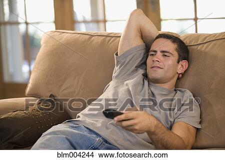 Hispanic man holding remote control on sofa View Large Photo Image Picture - Hispanic man holding remote control on sofa. Fotosearch