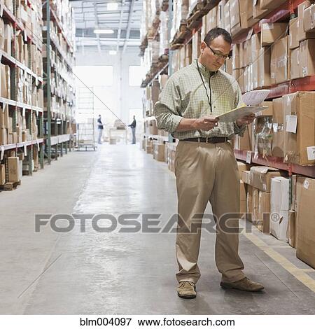 Stock Photo - Hispanic man looking at clipboard in warehouse. Fotosearch