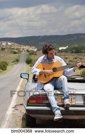Stock Photo - Hispanic man playing guitar on back of convertible. Fotosearch