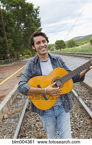 Hispanic man playing guitar on train tracks View Large Photo Image Stock Image - Hispanic man playing guitar on train tracks. Fotosearch