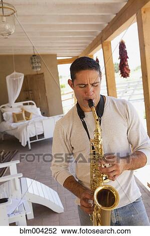 Stock Image - Hispanic man playing saxophone on patio. Fotosearch