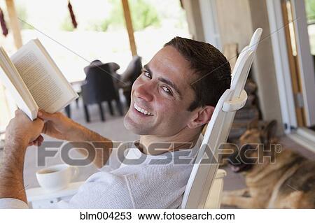 Stock Image - Hispanic man reading book on patio. Fotosearch