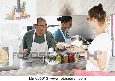 Stock Image - Hispanic man serving food in food cart. Fotosearch