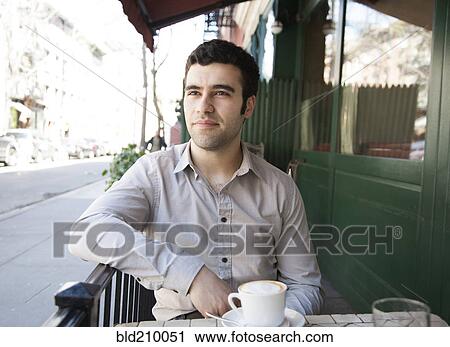 Stock Image - Hispanic man sitting at sidewalk cafe. Fotosearch