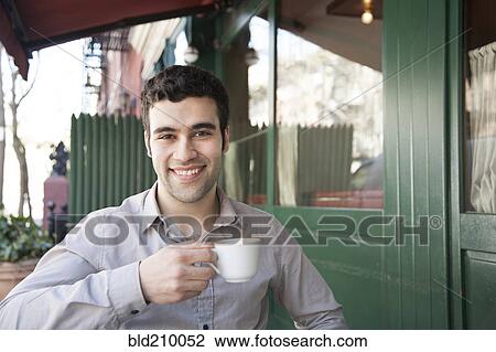 Stock Image - Hispanic man sitting at sidewalk cafe. Fotosearch