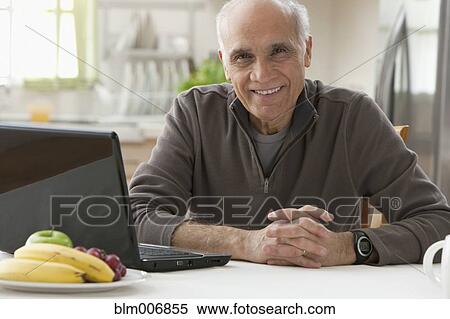 Hispanic man sitting in kitchen with laptop View Large Photo Image Stock Photography - Hispanic man sitting in kitchen with laptop. Fotosearch