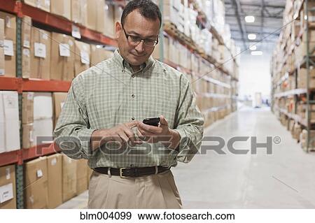 Hispanic man using cell phone in warehouse View Large Photo Image Stock Photo - Hispanic man using cell phone in warehouse. Fotosearch