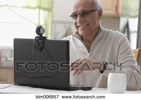Stock Photo - Hispanic man using laptop webcam in kitchen. Fotosearch