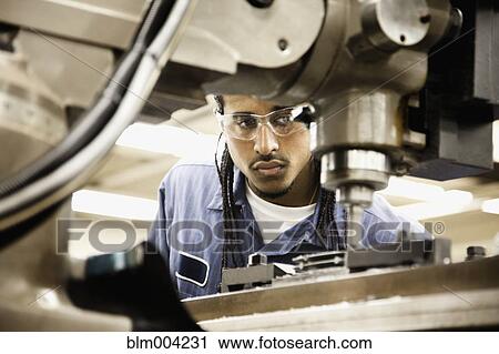 Stock Image - Hispanic man using machine in machine shop. Fotosearch