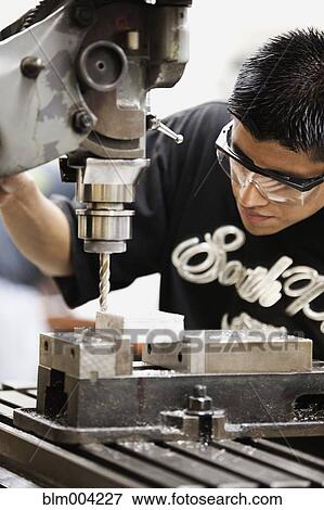 Stock Photo - Hispanic man using machine in machine shop. Fotosearch