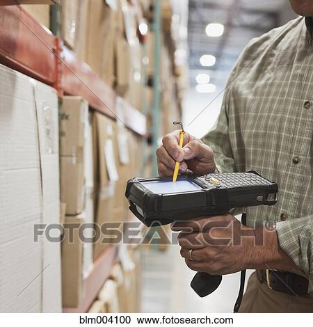 Stock Image - Hispanic man using tracking scanner in warehouse. Fotosearch