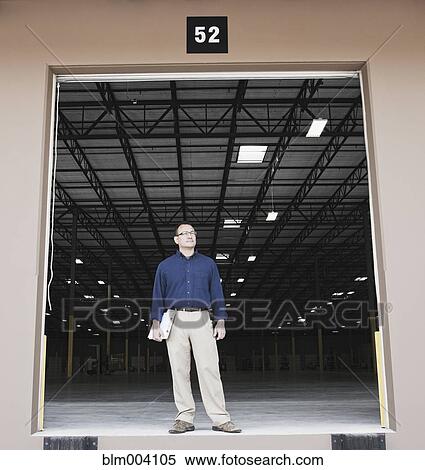 Stock Photography - Hispanic man with clipboard standing at warehouse loading dock. Fotosearch
