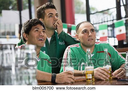 Stock Image - Hispanic men watching television in sports bar. Fotosearch