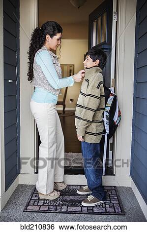 Stock Photograph - Hispanic mother zipping son's jacket at door. Fotosearch