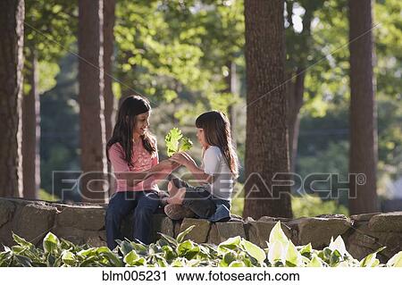 Stock Image - Hispanic sisters holding leaf. Fotosearch