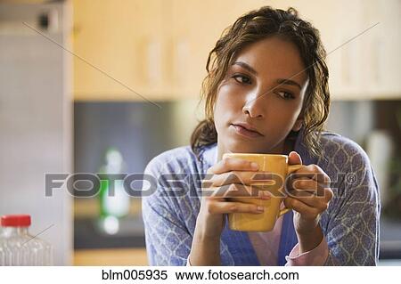 Stock Photography - Hispanic woman drinking coffee in kitchen. Fotosearch