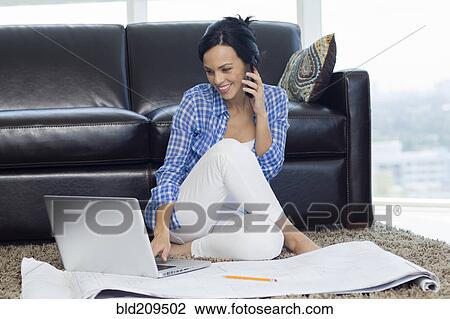 Stock Image - Hispanic woman examining blueprints in living room. Fotosearch