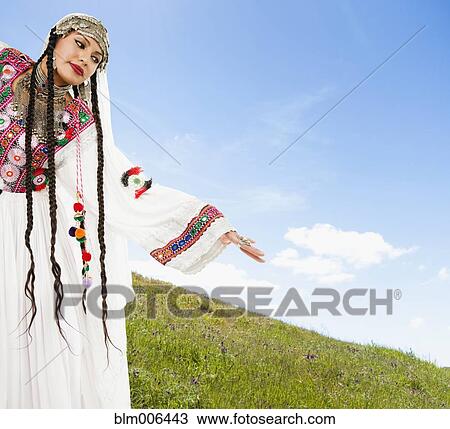 Stock Image - Hispanic woman in ornate headdress on hillside. Fotosearch