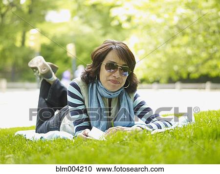 Stock Image - Hispanic woman laying on blanket in grass. Fotosearch