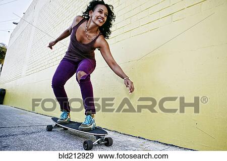 Hispanic woman riding skateboard on city street View Large Photo Image Stock Photo - Hispanic woman riding skateboard on city street. Fotosearch