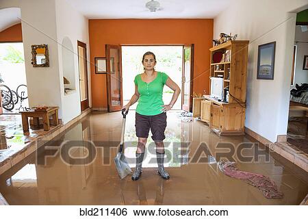 Stock Photograph - Hispanic woman shoveling water out of flooded house. Fotosearch