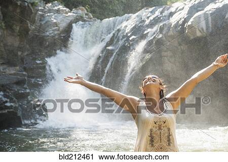 Stock Image - Hispanic woman standing by waterfall. Fotosearch
