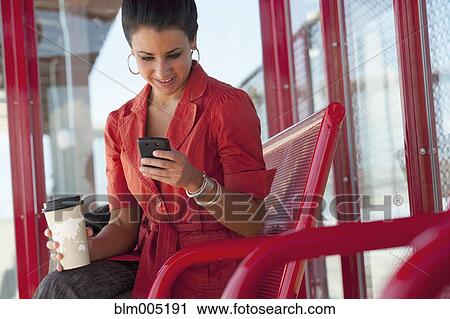 Stock Image - Hispanic woman using cell phone at bus stop. Fotosearch