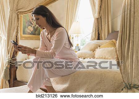 Stock Photograph - Hispanic woman using cell phone on bed. Fotosearch