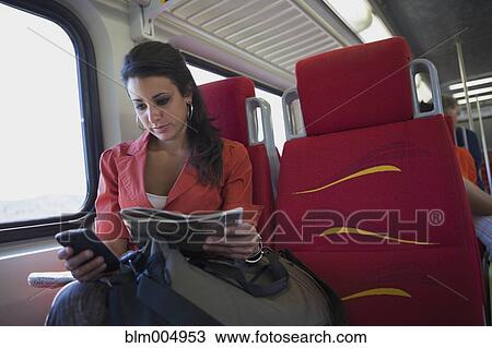 Stock Image - Hispanic woman using cell phone on train. Fotosearch