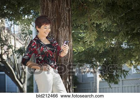 Stock Photograph - Hispanic woman using cell phone outdoors. Fotosearch