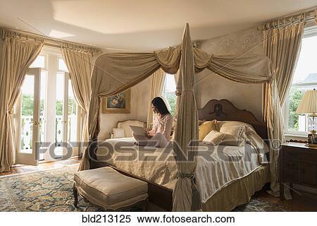 Stock Photography - Hispanic woman using laptop on bed. Fotosearch