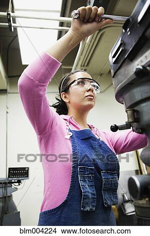 Picture - Hispanic woman using machinery in machine shop. Fotosearch