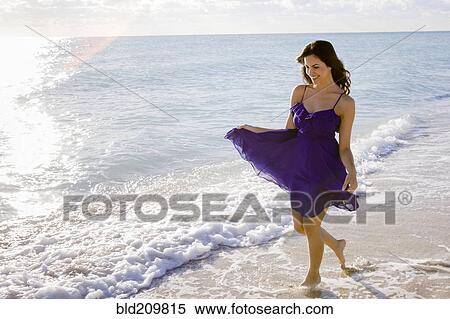 Stock Photography - Hispanic woman walking in surf on beach. Fotosearch