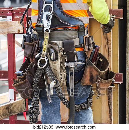Stock Image - Hispanic worker wearing tool belt at construction site. Fotosearch